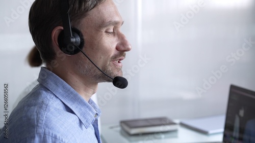 Happy smiling male call center operator in blue casual shirt is assisting clients online, providing customer support and answering inquiries. Business call center