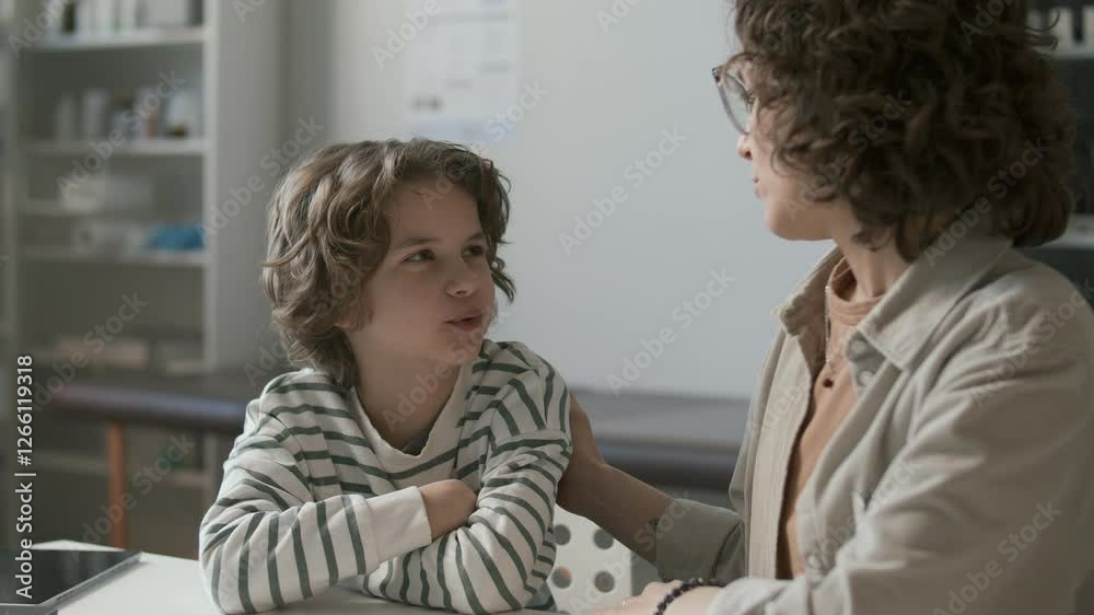 Caring mother talking to little son at desk in medical office, supporting and comforting child during health check-up Caring mother talking to little son at desk in medical office, supporting and comforting child during health check-up