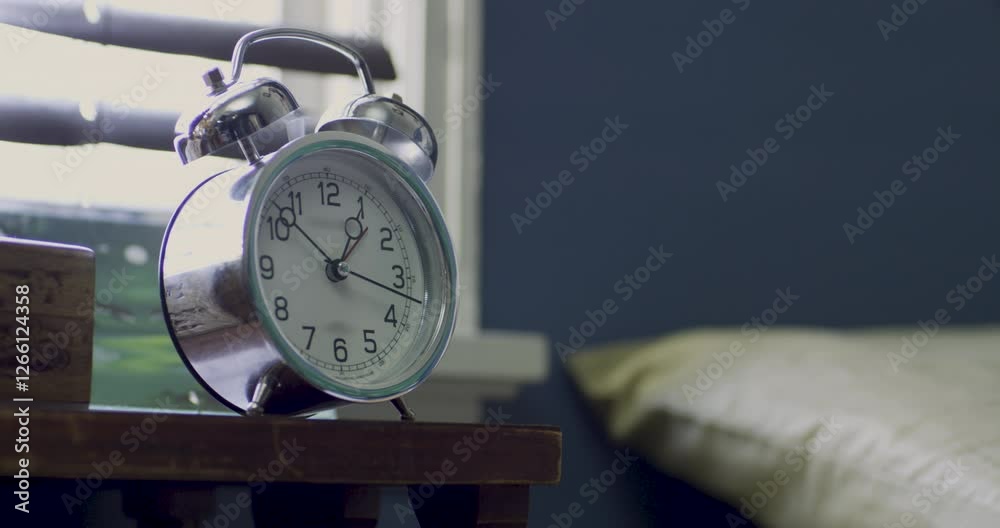 Hand reaching over from bed and grabbing ringing alarm clock, medium shot