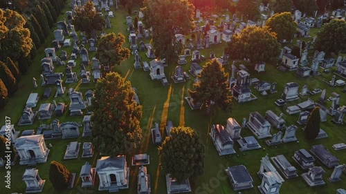 Slow Motion Aerial View of a Cemetery – Rows of Tombstones Aligned in a Serene Landscape, Soft Shadows Cast by Trees, Mist Gently Rising in the Distance, Peaceful and Reflective Atmosphere, Tranquil