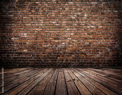 A rustic room features an aged brick wall with peeling plaster and a worn wooden floor.	