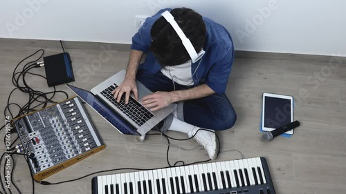 Young man in sound recording studio. Guy sit on floor and work with laptop and soung mixing console. Recording music. Microphone lying on tablet. Up view. photo