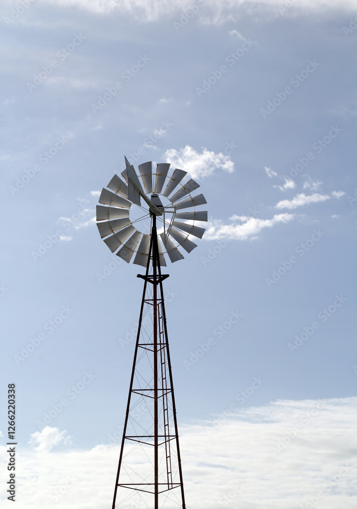 Windmill backlit against a blue sky with scattered clouds Windmill backlit against a blue sky with scattered clouds