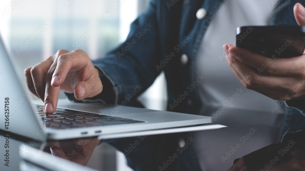 Closeup, business woman sitting at table using mobile smrt phone during working on laptop computer at home office. Young asian woman freelancer  surfing the internet, online working from home