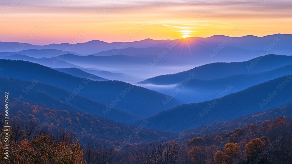 Obraz premium Majestic sunrise over layered blue mountains, showcasing autumn foliage and misty valleys.