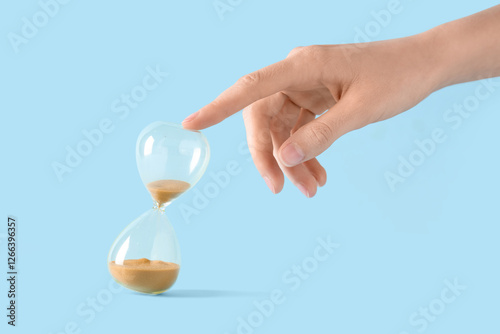 Female hand with yellow sand in stylish crystal hourglass on blue background
