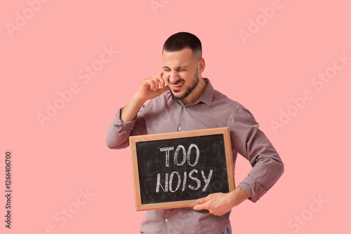 Irritated young man holding chalkboard with text TOO NOISY on pink background