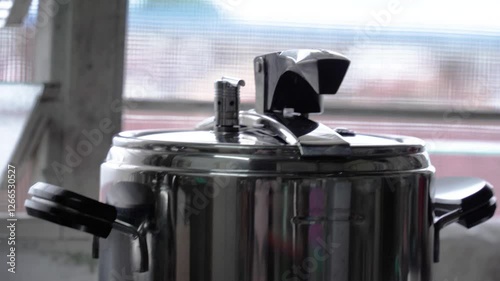A close-up view of the steam and vapor from a pressure cooker vividly captures the rising, swirling mist that escapes from the cooker’s valve or lid during cooking. 