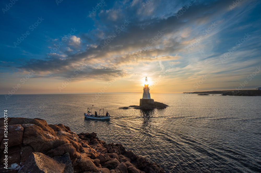 lighthouse at dusk with a boat passing by lighthouse at dusk with a boat passing by