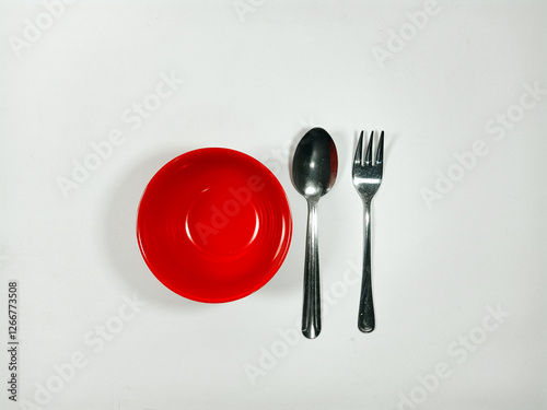 A red bowl and a silver fork are placed on a white background. The bowl is empty, and the fork is bent. Concept of emptiness and simplicity, with the focus on the basic elements of a meal