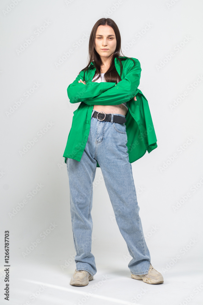 Fototapeta premium Cute young girl in green shirt and blue jeans posing on a white background