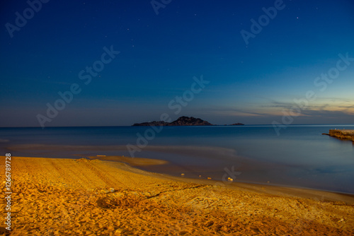 Fototapeta Naklejka Na Ścianę i Meble -  Tranquil seascape featuring a beach in the foreground, calm water, and a distant island under a night sky.Arillas, Corfu island, greece, 
