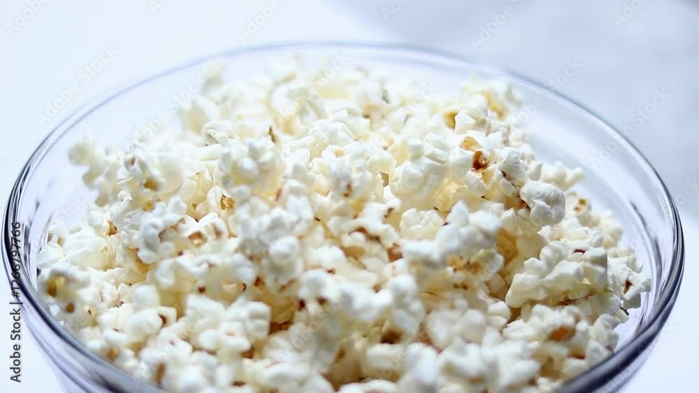 Close up of female hand taking tasty popcorn from a glass bowl on white table background Close up of female hand taking tasty popcorn from a glass bowl on white table background