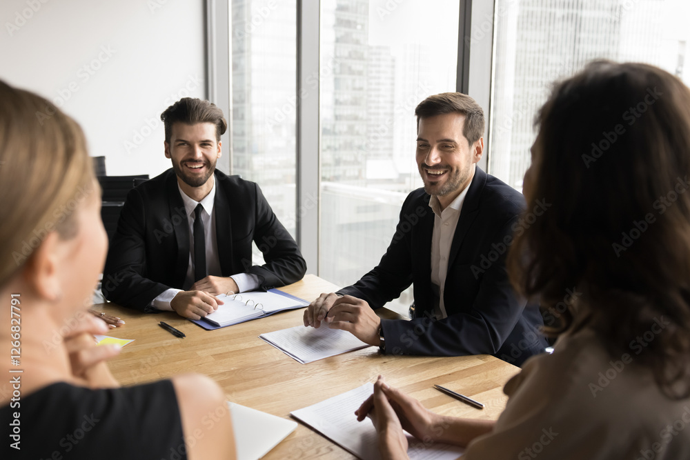 Group of four businesspeople gathered at conference table, engaged in lively, positive discussion, looks satisfied with successful meeting results, good collaboration while planning future strategy