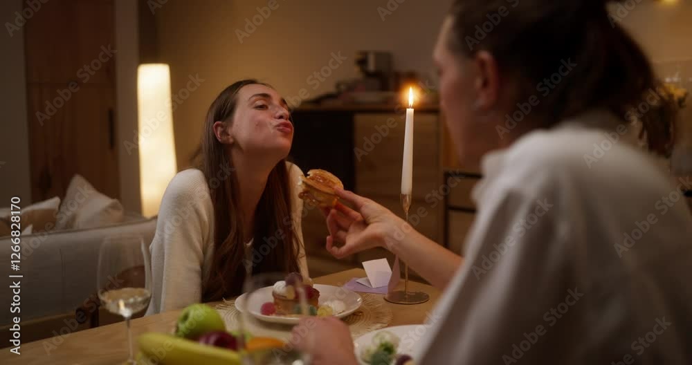 Over his shoulder a guy in a white shirt feeds his girlfriend delicious sweet pastries during a romantic dinner at home in the evening Over his shoulder a guy in a white shirt feeds his girlfriend delicious sweet pastries during a romantic dinner at home in the evening