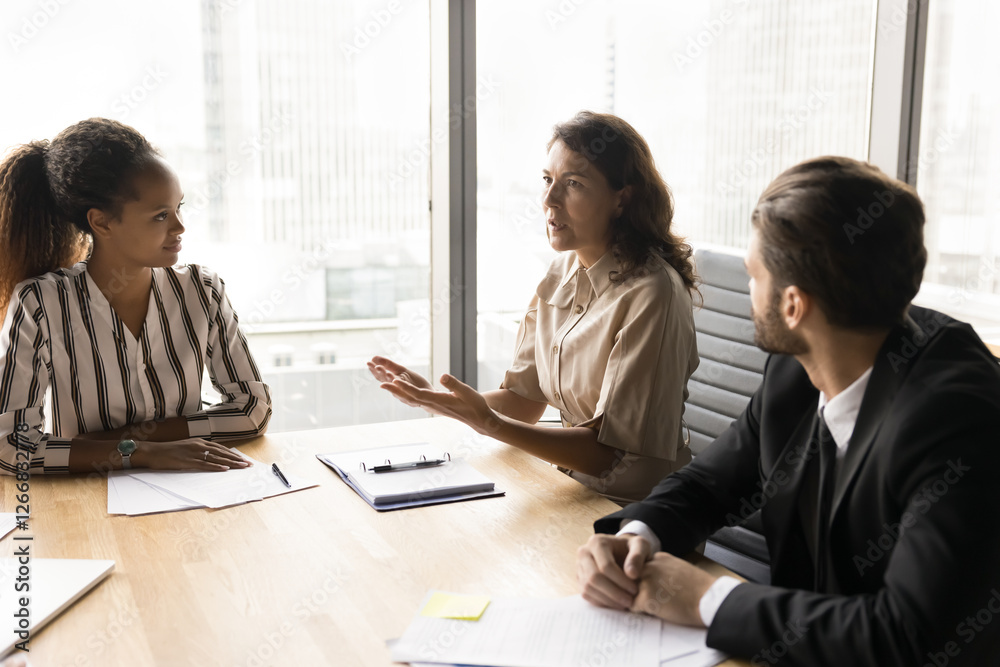 Three business professionals seated in conference room engaged in discussion, focused on strategizing or problem-solving, making decisions regarding upcoming market opportunities, resources allocation Three business professionals seated in conference room engaged in discussion, focused on strategizing or problem-solving, making decisions regarding upcoming market opportunities, resources allocation