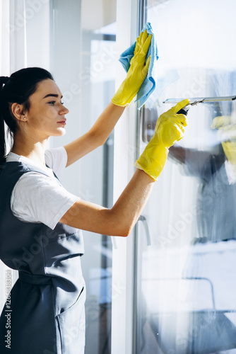 Female housekeeper wearing yellow gloves washing windows