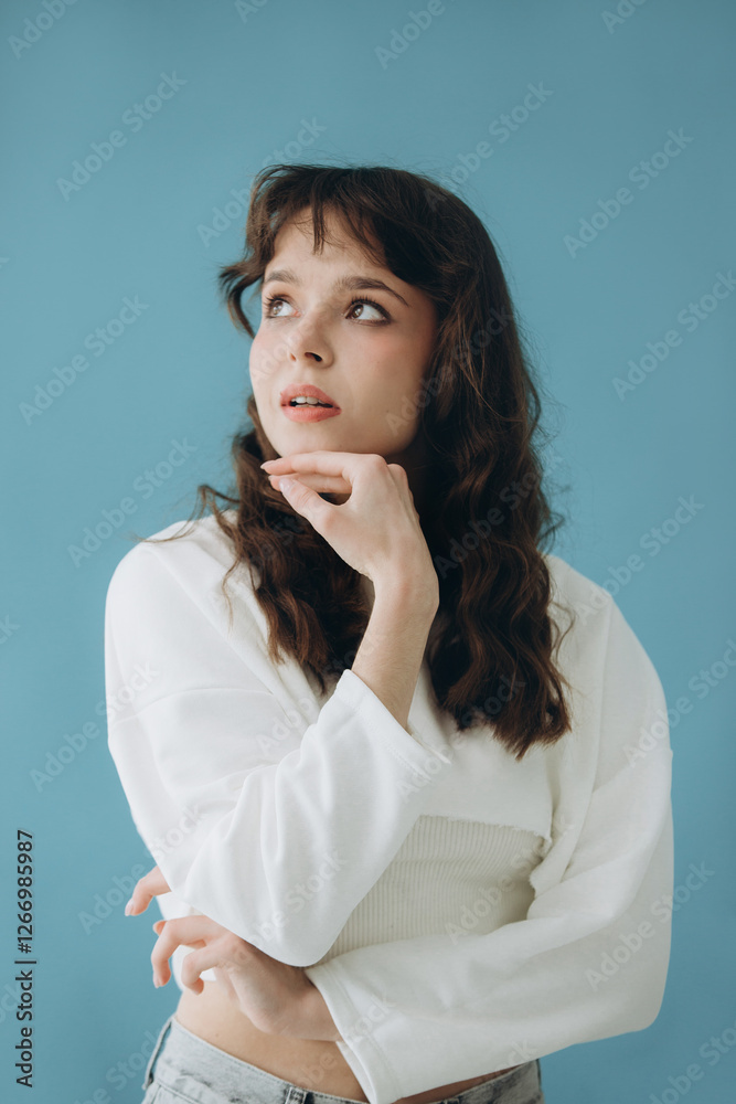Young Woman in Casual Clothing Posing Thoughtfully Against Blue Background Young Woman in Casual Clothing Posing Thoughtfully Against Blue Background