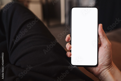 Man hold smartphone with white screen in his hand sitting on a couch in home environment