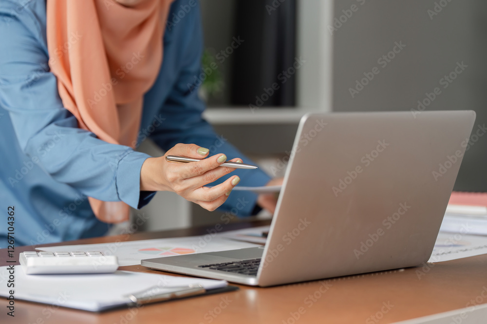 Diverse Muslim woman analyzing data on laptop while preparing financial report. Diverse Muslim woman analyzing data on laptop while preparing financial report.
