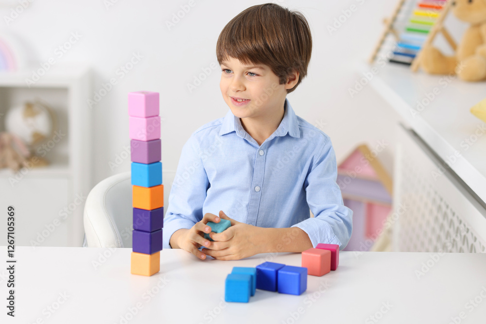 Happy boy with tower of colorful cubes at table indoors Happy boy with tower of colorful cubes at table indoors