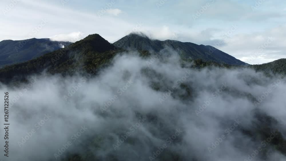 Aerial view of beautiful mountain peak with lush green tropical forest in morning mist. Clouds move in the wind at Puncak Bogor. Aerial view of beautiful mountain peak with lush green tropical forest in morning mist. Clouds move in the wind at Puncak Bogor.