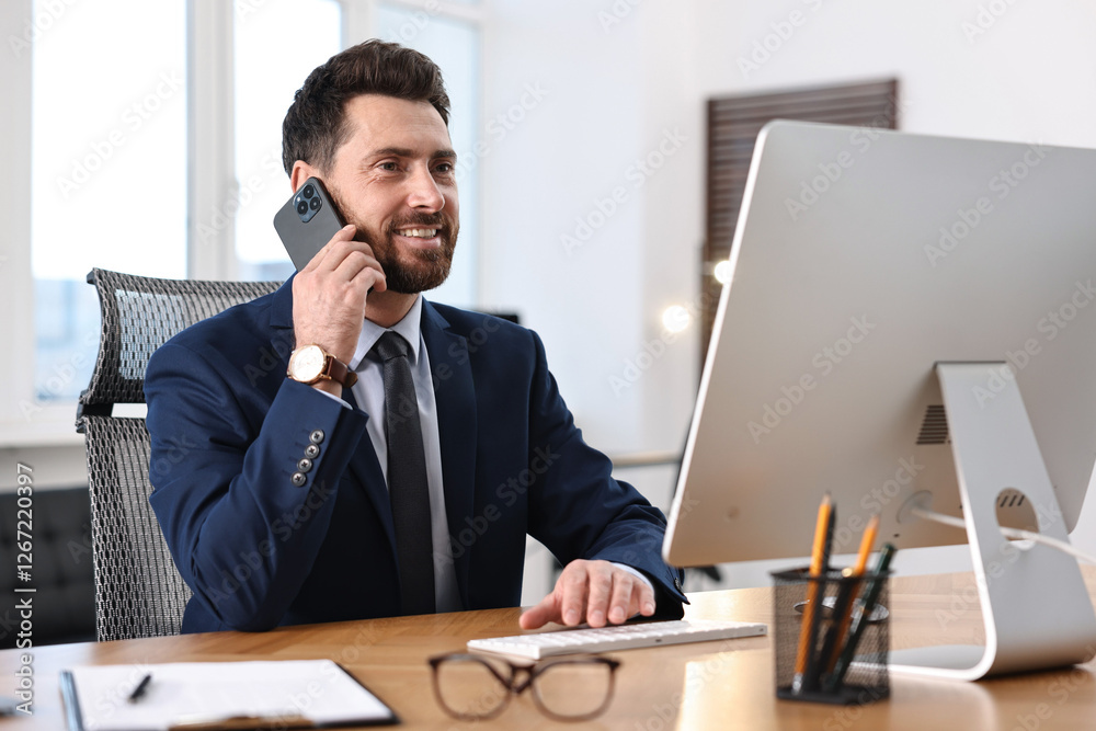 Man talking on smartphone while working with computer at table in office Man talking on smartphone while working with computer at table in office