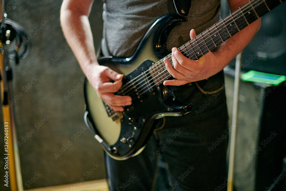Obraz premium Musician playing an electric bass guitar at music rehearsal, practicing guitar technique in dimly lit setting, close up view guitarist hands