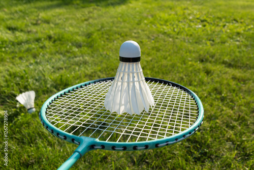 White badminton shuttlecock and badminton rackets on green grass in sunny shadow. Summer. Leisure games. Outdoors. Close up.