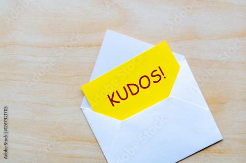 KUDOS text on yellow notepad inside an envelope. Achievement concept