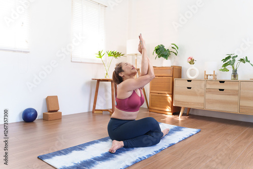 Senior Asian woman practicing Urdhva Hastasana Upward Salute Pose on a yoga mat in a cozy home setting photo
