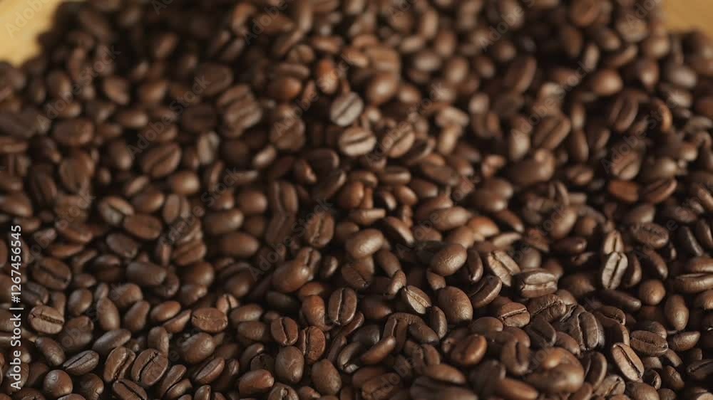 A person is pouring coffee beans into a cup. The coffee beans are scattered all over the table