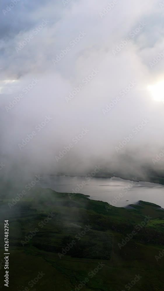 Clouds drift over lush landscape and tranquil lake in evening light capturing nature's serene beauty.