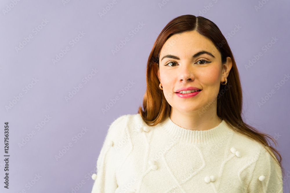 Fototapeta premium Cheerful young woman smiling and wearing a white sweater on a purple background