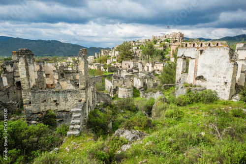 Abandoned stone houses of Kayaköy ghost town village surrounded by green spring nature under a stormy sky, Fethiye, Turkey