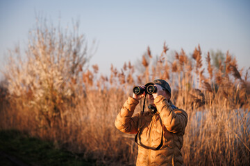 Bird watching. Woman biologist with binoculars observes wildlife animals and water birds in nature habitat