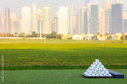 A pyramid stack of golf balls on a green turf with a modern city skyline in the background, blending sports and urban living. Pyramid of Golf Balls with City Skyline photo