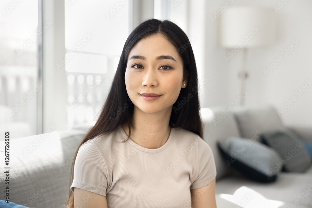 Head shot portrait pretty Asian young woman sitting in cozy, sunny, well-lit room, looking at camera with peaceful, serene expression. Confidence, modern lifestyle, home comfort, personal well-being Head shot portrait pretty Asian young woman sitting in cozy, sunny, well-lit room, looking at camera with peaceful, serene expression. Confidence, modern lifestyle, home comfort, personal well-being