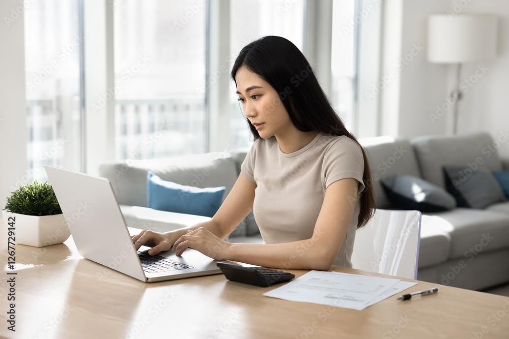 Focused Asian woman sit at table in living room, busy in personal expenses management, calculate household utilities, pay taxes, bills through secure e-banking system on computer. Finances, accounting Focused Asian woman sit at table in living room, busy in personal expenses management, calculate household utilities, pay taxes, bills through secure e-banking system on computer. Finances, accounting