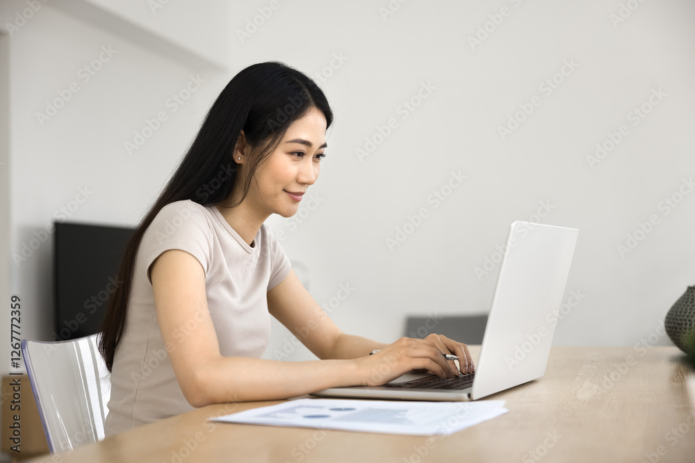 Young Asian woman sitting at desk, working intently on laptop, engage with her on-line tasks at home, studying using education platform, looks focused while read document, analyze data, do research Young Asian woman sitting at desk, working intently on laptop, engage with her on-line tasks at home, studying using education platform, looks focused while read document, analyze data, do research