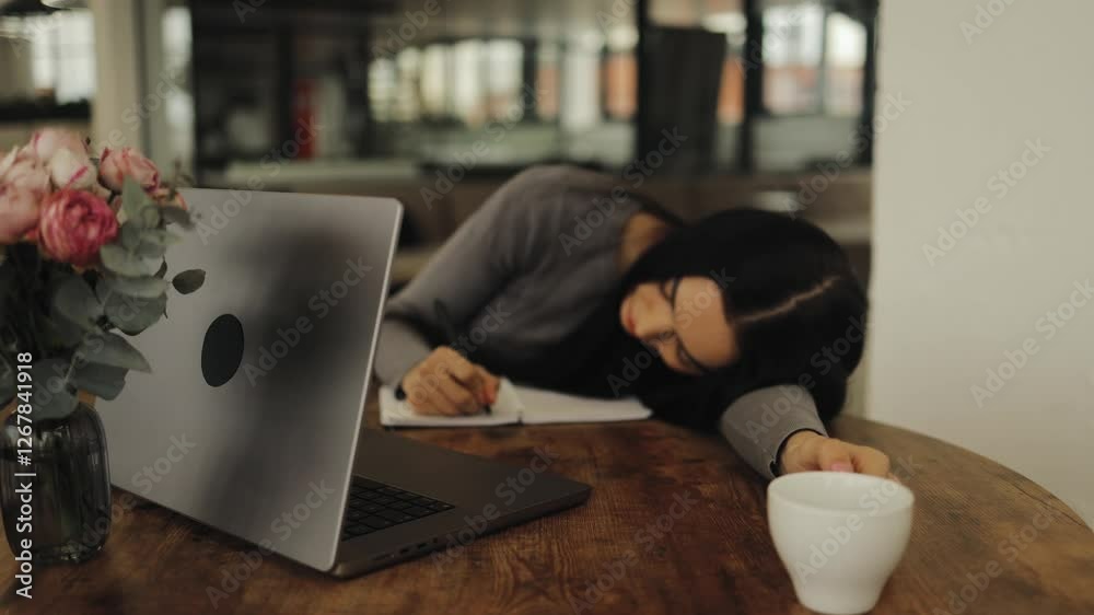 Tired working woman, student lying on the table and taking a break from work, chilling, taking notes, laptop, remote work, relaxation, break, reflection, despondency, boredom, caffeine, cafe, drink