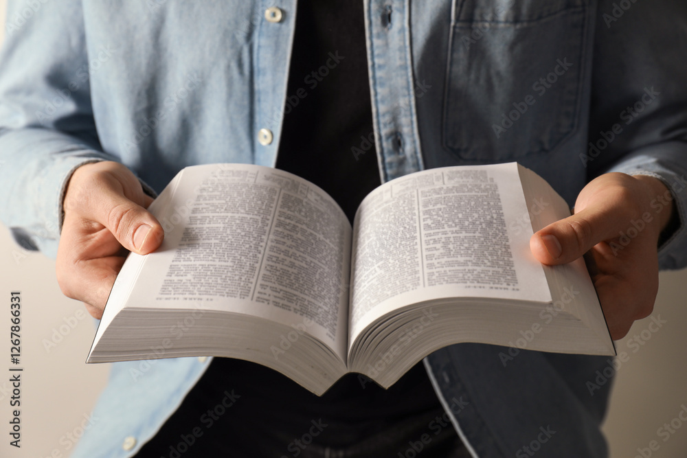 Fototapeta premium Man reading Holy Bible in English language on light background, closeup