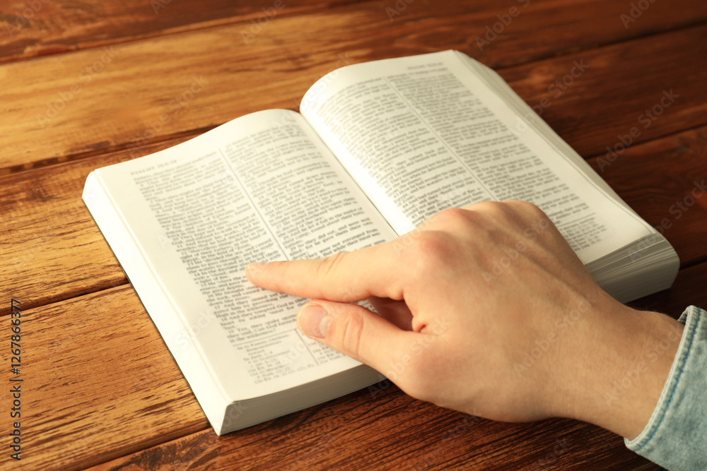 Naklejka premium Man reading Holy Bible in English language at wooden table, closeup