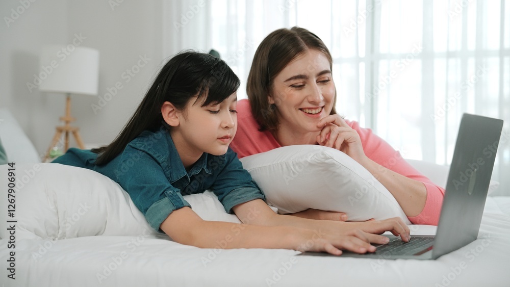 Attractive daughter and caucasian mother watching movie at laptop screen while lie on bad. Happy family spend time together before bed time. Parent and cute girl enjoy playing games together Pedagogy. Attractive daughter and caucasian mother watching movie at laptop screen while lie on bad. Happy family spend time together before bed time. Parent and cute girl enjoy playing games together Pedagogy.