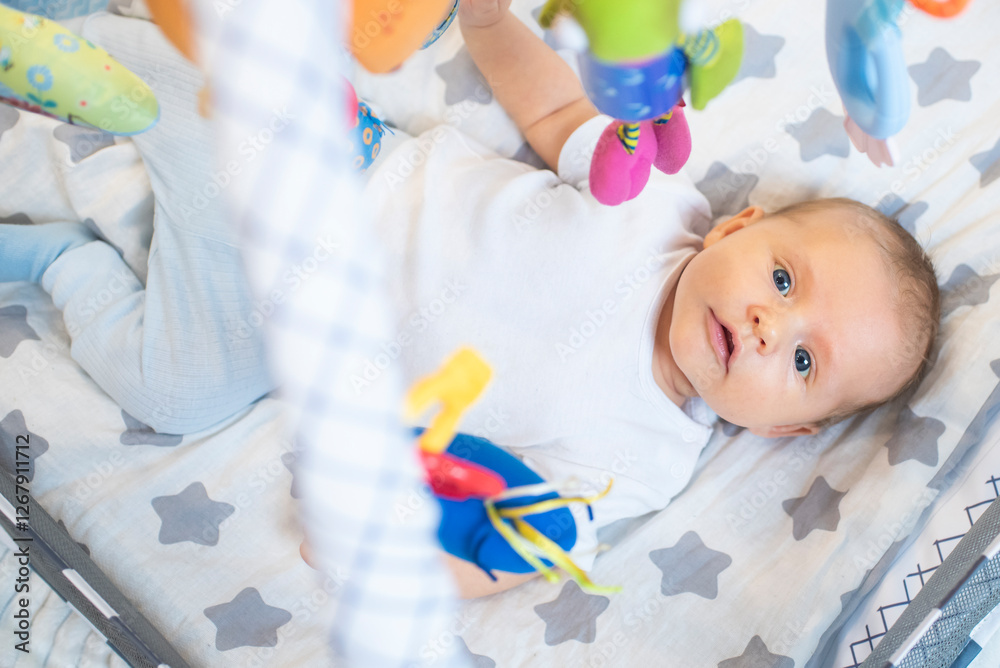The baby lies on a development mat, above the child on arches hang colored toys with different textures and properties. The boy looks at the toys and pushes them with his hand. The child is 1.5 months The baby lies on a development mat, above the child on arches hang colored toys with different textures and properties. The boy looks at the toys and pushes them with his hand. The child is 1.5 months