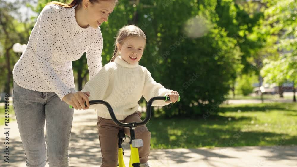 Woman is helping a young girl ride a bike. The girl is smiling and seems to be enjoying the experience. The scene is set in a park, with trees. happy family. girl mother park. woman child kid walk Woman is helping a young girl ride a bike. The girl is smiling and seems to be enjoying the experience. The scene is set in a park, with trees. happy family. girl mother park. woman child kid walk