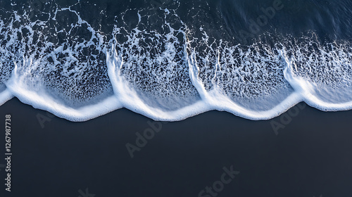 Aerial view of dark sand meeting the sea white foam creating rhythmic patterns along the shoreline.