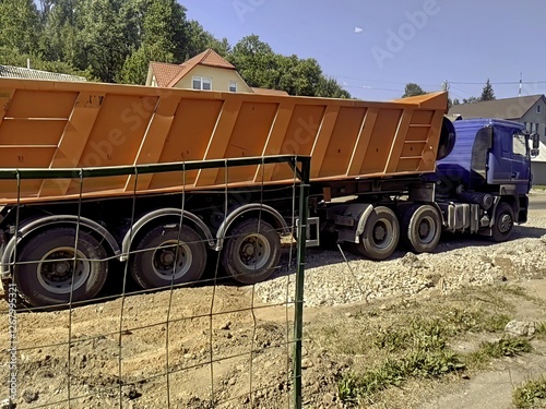 The image shows a dump truck parked on a construction site. The truck has a blue cab and an orange self-dumping body. Surrounding the truck are elements of construction


Ask

Explain




