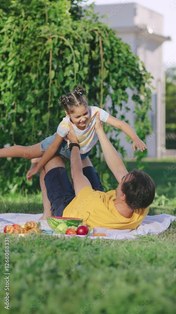 Vertical video father and daughter enjoys a lively picnic in a sunny park with fresh fruits while a child playfully interacts with an adult Vertical video father and daughter enjoys a lively picnic in a sunny park with fresh fruits while a child playfully interacts with an adult