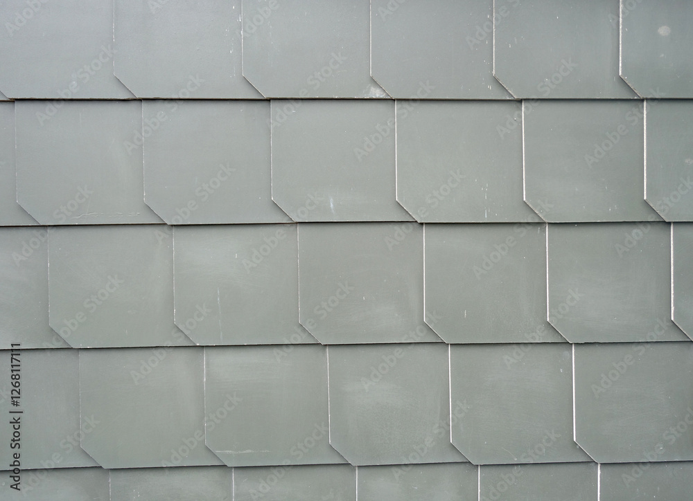 Naklejka premium The image shows a close-up of a wall made up of gray tiles. The tiles are arranged in a grid-like pattern, with each tile having a hexagonal shape. The texture of the tiles is rough and uneven
